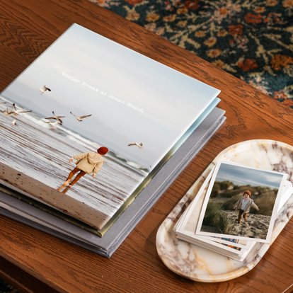 A closed binder slip-in photo album with a custom photo cover sitting on a coffee table next to a stack of photo prints.