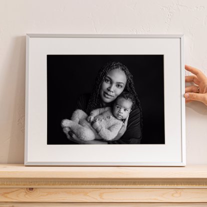 Framed Print of a mother holding her newborn daughter in black and white with a thin white frame and a mat.