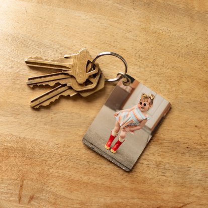 metal photo keychain sitting on a wood table with a photo of a young girl posing wearing sunglasses 