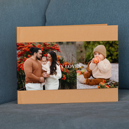 A closed premium hardcover photo book with a caramel colored linen cover and a skinny dustjacket featuring two photos from a Fall family portrait session.