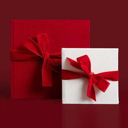 A 12x12 hardcover photo book with a red linen cover and an 8x8 white leather photo album wrapped in red velvet bows.