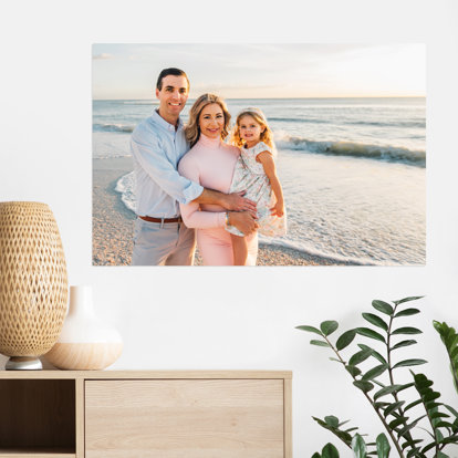 A large metal print hanging on the wall featuring a photo of a family on the beach. 