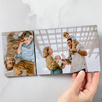 A hand holding a tabletop hinged print from Mpix featuring photos from a family picture session.