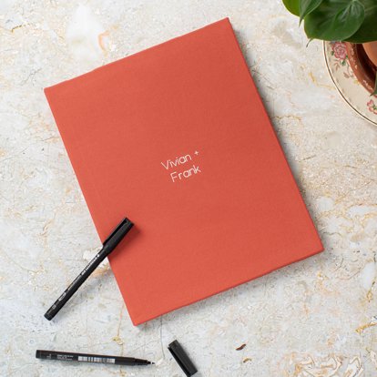 A closed photo book with a linen cover and gold foil debossed text that reads Vivian + Frank.