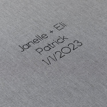 A close up image showing the black foil debossing on a graphite gray linen cover that reads "Janelle + Eli Patrick 1/1/2023" in personalized text.
