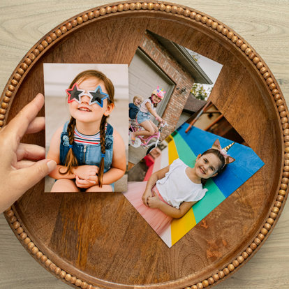 Three colorful 4x6 photo prints laid out on in a wooden tray each featuring a young girl outside enjoying summer.