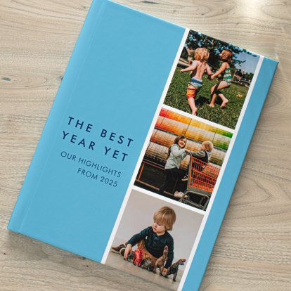 A closed hardcover photo book with a blue background and a film strip of three photos featuring a brother and sister. The text on the front cover says 'The Best Year Yet, Our Highlights from 2025'.