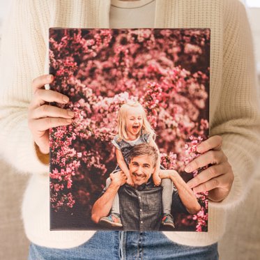 Woman holding an Mpix Canvas Gallery Wrapped Print of a father and daughter playing in front of a tree.