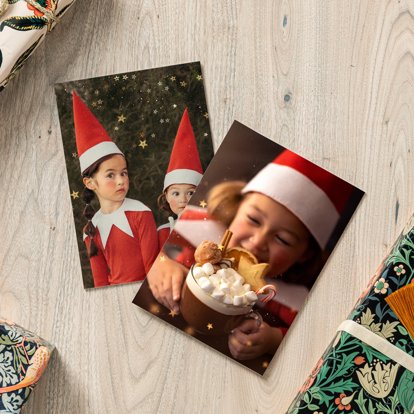 Two photo prints laying on a table and featuring images of children in Christmas outfits.