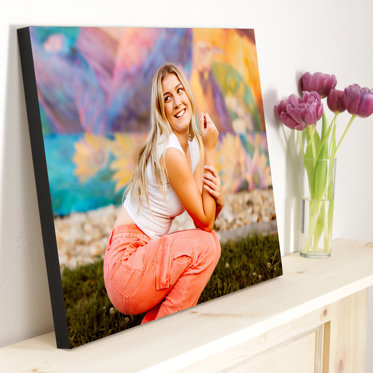 Standout photo print from Mpix resting against the wall on a mantle next to a vase of purple flowers with a senior portrait of a girl with a colorful wall behind her..