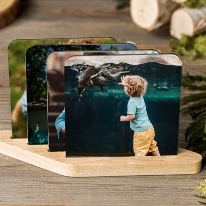 A set of personalized photo coasters stored and displayed in a wooden coaster stand.