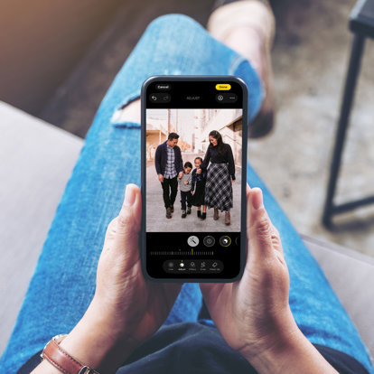 Hands holding a phone so you can see the screen. The screen shows someone editing a photo of family standing outside in the street. 