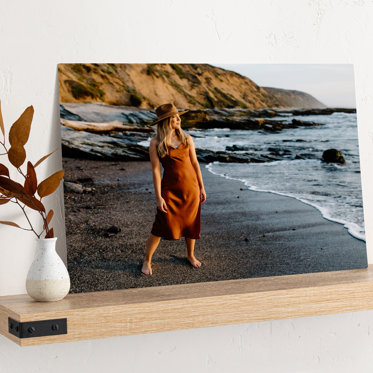 Metal photo print from Mpix leaning against the wall on a wood block showing a girl in a dress standing on the sand the beach in the wake of the ocean for her senior photos. 