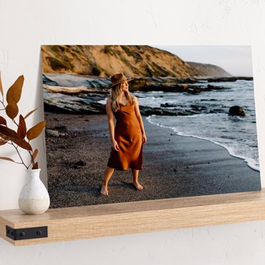Metal photo print from Mpix leaning against the wall on a wood block showing a girl in a dress standing on the sand the beach in the wake of the ocean for her senior photos. 
