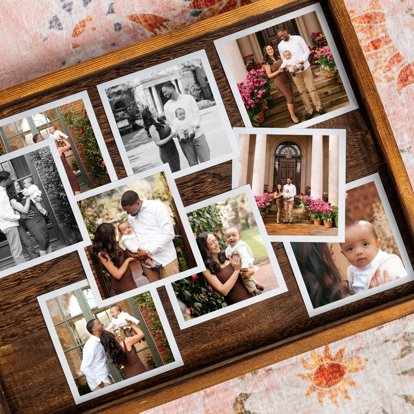 A signature print set featuring photos of a mother and father with their baby boy. The pictures have a white border and are scattered on a wooden tray. 