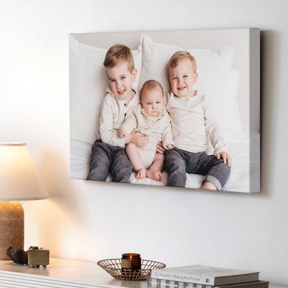 A large canvas print featuring a photo of two young kids with their new baby brother. The canvas print is hanging above a side table.