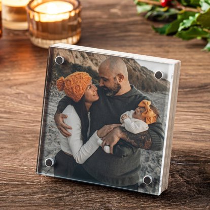 A square birch photo block from Mpix displayed on a table featuring a mom and dad with their new baby outside.