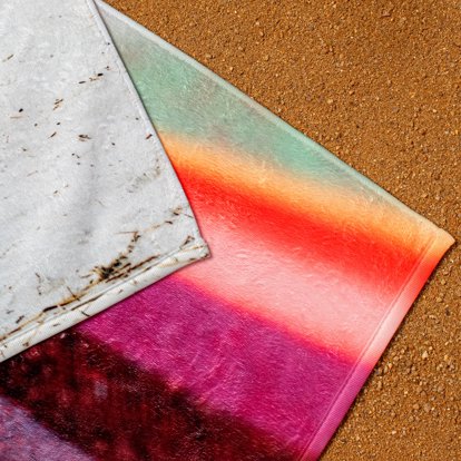 A close-up image on the corners of several personalized towels laying in the sand on a beach.