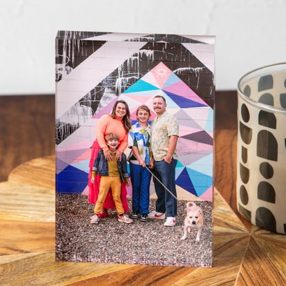 A vertical acrylic photo block featuring a family of four and their dog standing in front of a colorful wall display.