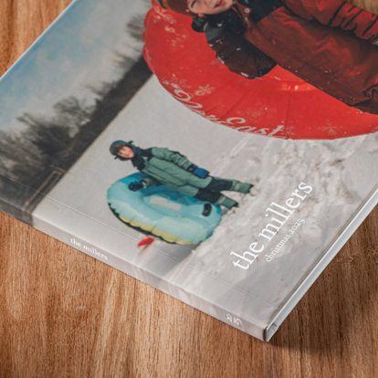 A custom cover photo book laying on a wood table and featuring a photo of children holding intertubes in the snow.