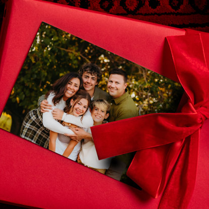 A 4x6 photo print of a family set atop a present wrapped in red wrapping paper with a red velvet bow. 
