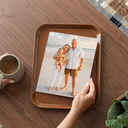 An 8x10 photo print of a couple with their grandbaby standing on a sandy beach. The print is set on a brown tray on a table.