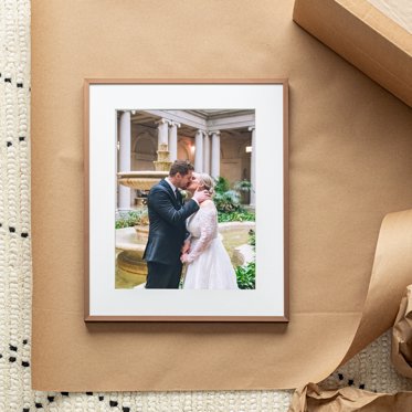 A Framed Photo Print from Mpix sitting on Kraft of a couple kissing on their wedding day, with a white mat and thin wooden frame. 
