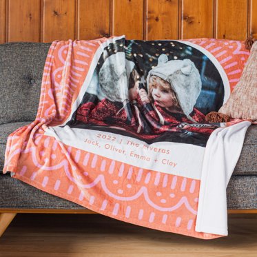 A personalized blanket from Mpix draped over a couch with salmon colored background with a light alternating scallop and dashed pattern and featuring a holiday image. 