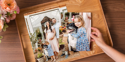 Family photo prints displayed in a wooden keepsake box on a tabletop with flowers