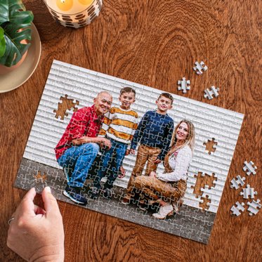 A hand assembling a photo puzzle from Mpix on a wooden table.