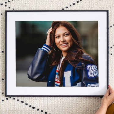 Framed print from mpix featuring a white mat and thin metal frame, the photo is of a young athlete in her letter jacket. 