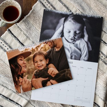 two types of wall calendars are laid out to show the different binding options, one with a hook on top for hanging and the other with a pre punched hole