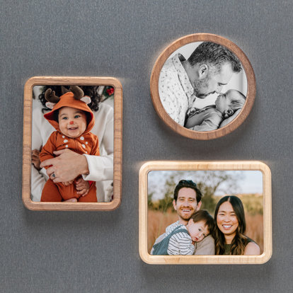 Three framed magnets displayed on a fridge. One is circular, the other two are rectangular shaped. The circle magnet features a family photo of mom and dad holding their toddler boy. One rectangle framed magnet features a baby in a reindeer costume. The other is of mother and father holding their young son.