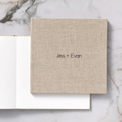 A closed photo book with a tan linen cover and debossed text in black foil that reads "Jess + Evan" on top of an open photo book with images and blank space for guest book signatures.