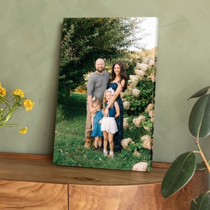 A wrapped canvas print standing up on a wooden table featuring a posed image of a family in a field.