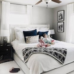 A parent and child resting on a made bed, framed black-and-white prints above