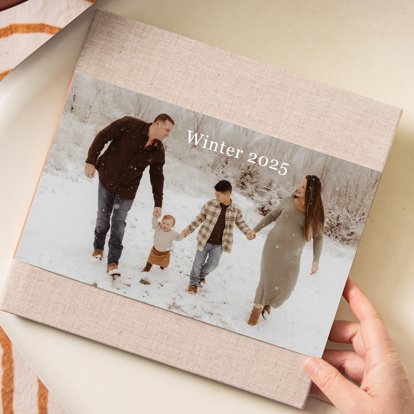 A photo book with tan linen hardcover and a dustjacket featuring a photo of a family walking in the snow.