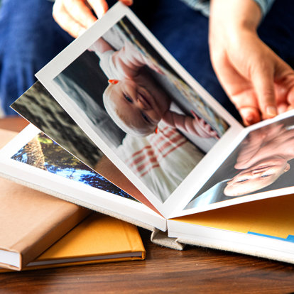 Close up view of hands flipping through a photo book with thick, layflat pages & a linen cover featuring photos of a smiling baby.