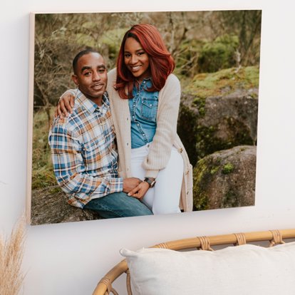a print on wood hanging in the bedroom of a couple posing for a photo in the forest. 