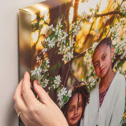 An up close shot of the corner of a canvas print hanging on the wall. The print features two sisters standing by a magnolia tree.