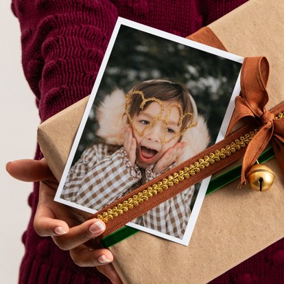 A person's hands hold a wrapped holiday gift with a photo print included in the packaging.