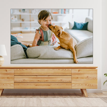 A large framed textile print with an image of a dog licking a girl's face that is hung above a desk.