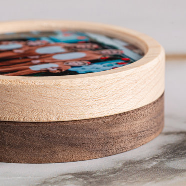 Close up shot of the walnut and maple frame finishes on two stacked circular framed photo magnets.