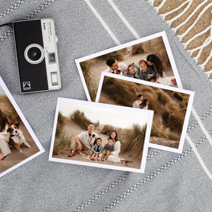 4x6 photo prints scattered on a blue woven tablecloth featuring a young couple with their two boys and dog at the beach. 