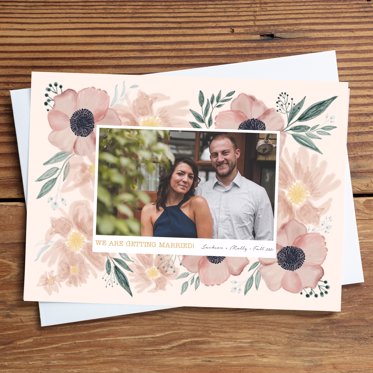 Save the Date card from Mpix resting on a white envelope with a rectangular photo surrounded by flowers and personalized wedding details. 