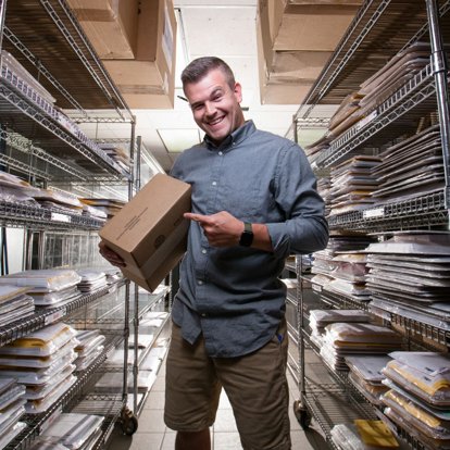 A lab team member holding a packed order box in the shipping racks, surrounded by orders waiting to go out