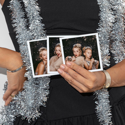 Hands holding three photo prints featuring two sisters dressed up for a New Year's party and wearing 'Happy New Year' headbands. 