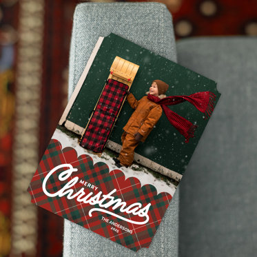 A Christmas photo card featuring a boy standing in the snow with a toboggan.