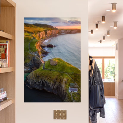 A large metal print hanging on the wall featuring an overhead shot of the bluffs that meet the shoreline with the sun setting in the distance.