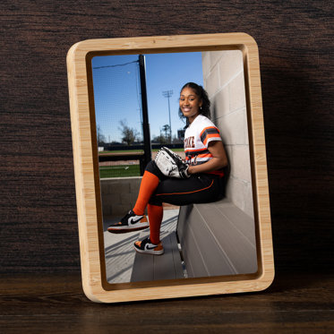 A tabletop framed metal print featuring an image of a senior softball player sitting in the dugout.